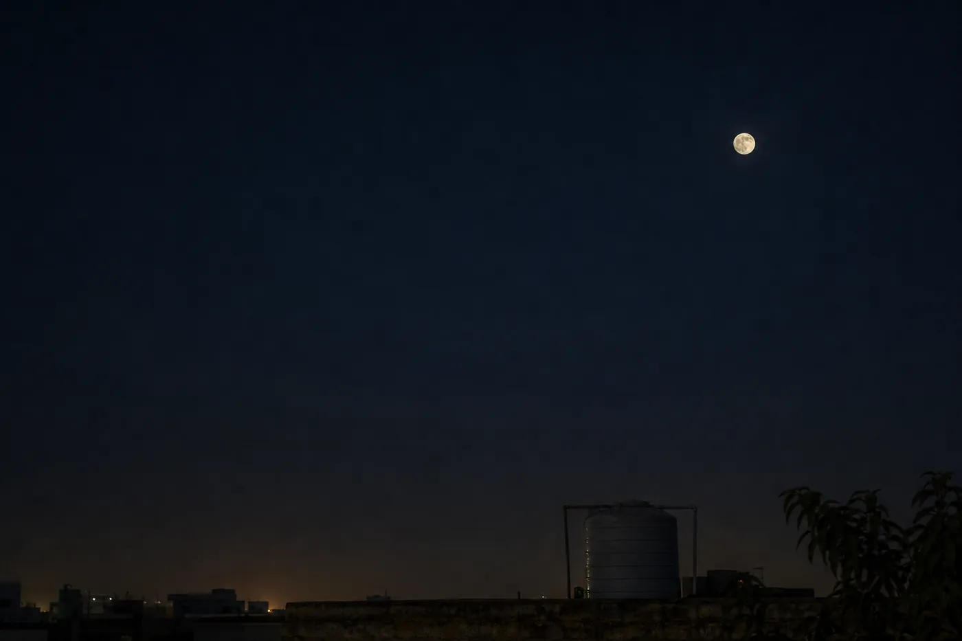 Photorealistic illustration of a small Full Moon above an anonymous Delhi rooftop at night